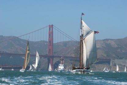 The scow schooner ALMA with sails set, running with the wind on San Francisco Bay, with the Golden Gate Bridge and Marin Headlands in the background.