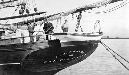 The stern of a lumber schooner with two men and a woman standing on the deck.
