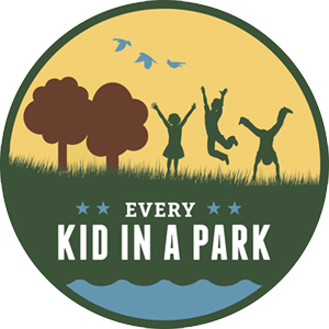 A round logo with trees and kids jumping.