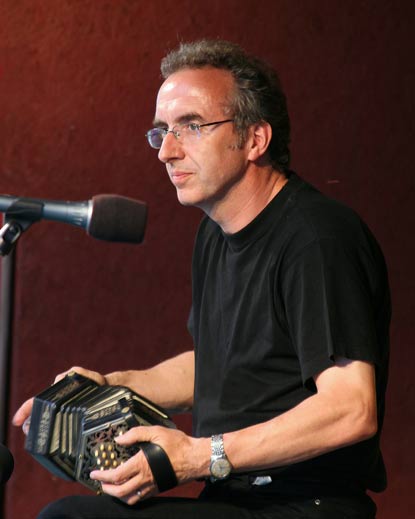 A man seated in front of a microphone and holding a musical instrument that looks like a small accordion.