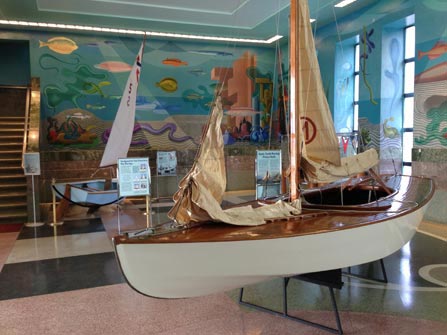 An exhibit of boats, text panels and colorful murals in the lobby of a building.