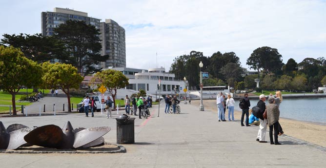 People standing on a cement walkway near the San Francisco Bay in Aquatic Park.