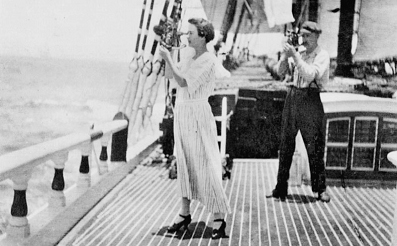 A woman standing on the deck of a 19th century sailing ship using a sextant to take a sight.