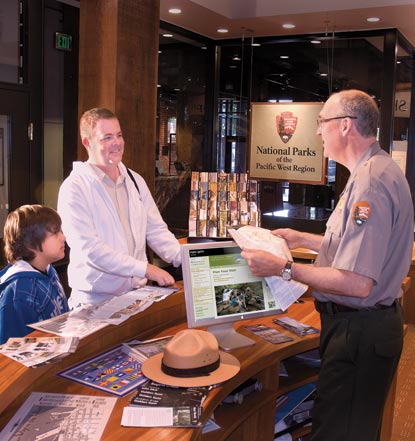 A park ranger standing behind a desk talking with visitors.