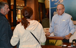 A man standing behind an information desk talking with two park visitors.