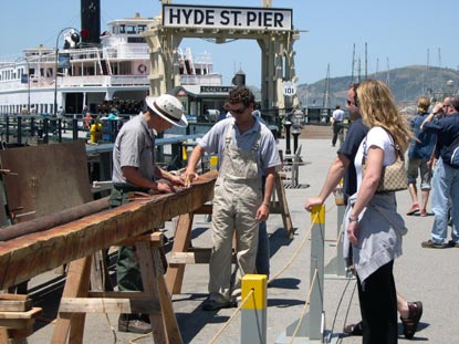 People on Hyde Street Pier working on a spar (mast) for a boat.