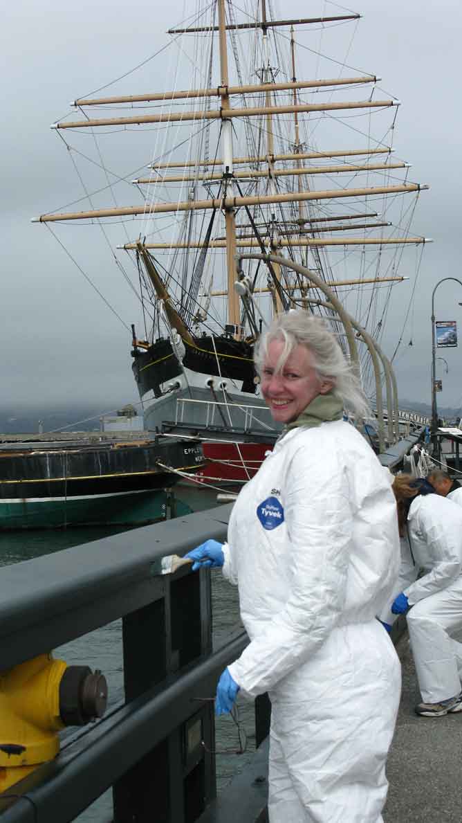 A woman in a white jumpsuit painting a pier railing.