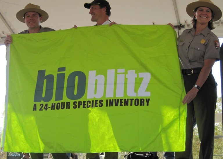 Three people hold a flag with text "bioblitz: a 24-hour species inventory."