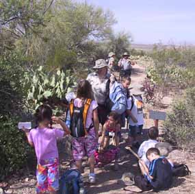 Park service rangers & volunteer naturalists stand with students on a trail.