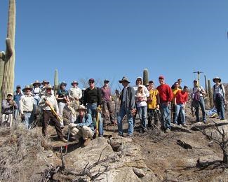 A group of people with tools and sun hats stand in a desert setting.