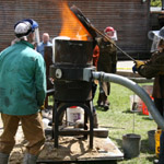Fire spews forth from a small cylindrical furnace as fuel is loaded in the top.