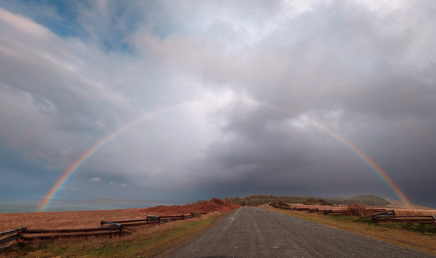 color photo of a gravel road with a rainbow in the center