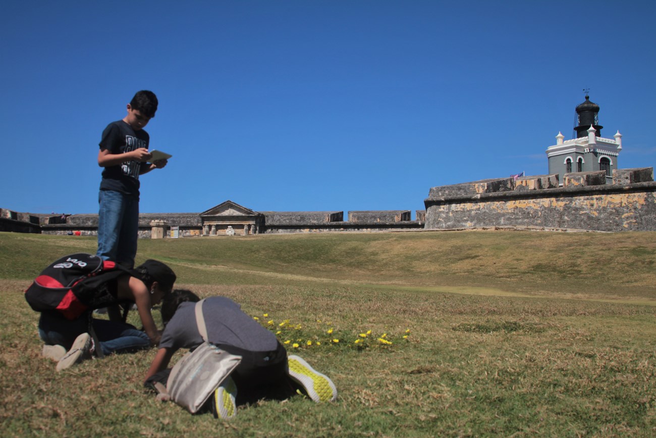 Three students work on an assignment in front of El Morro.