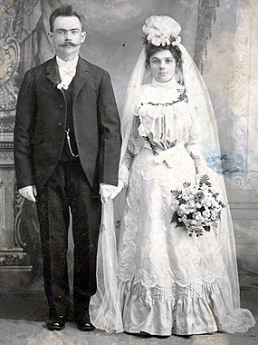 wedding portrait; groom is wearing a suit and bride is wearing a floor length gown with a long veil.