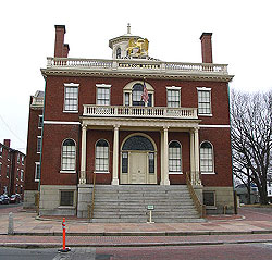 The Custom House is a large, square two story building with a cupola in the middle of the roof and a large portico over the grand stairs that sweep up to the front door.