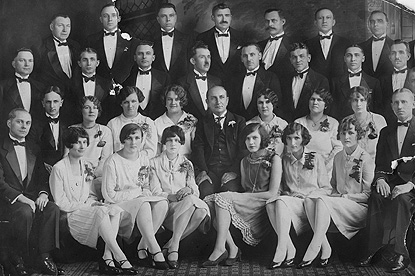 A group of men and women in tuxedos and gowns in a formal portrait