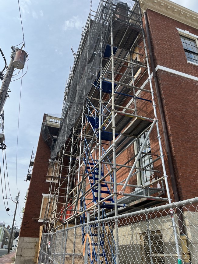 Large scaffolding extends to the roof of a large brick building.