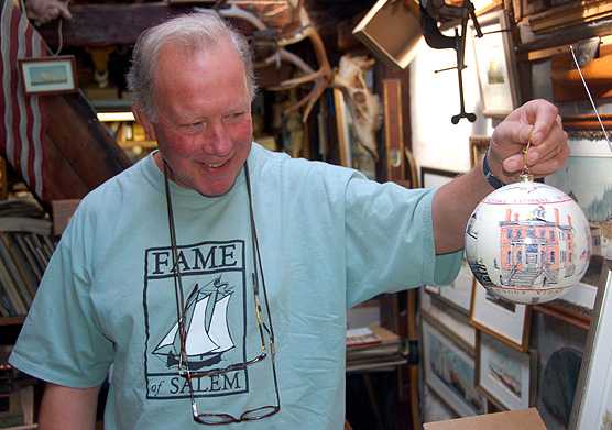 Salem artist Racket Shreve holding up a 6 inch diameter ornament decorated with buildings at Salem Maritime