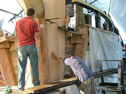 two men glueing a layer of wood onto the structural timbers on the front of the ship