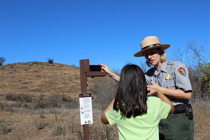 Ranger interacts with a youth and demonstrates how to use a photo-monitoring station