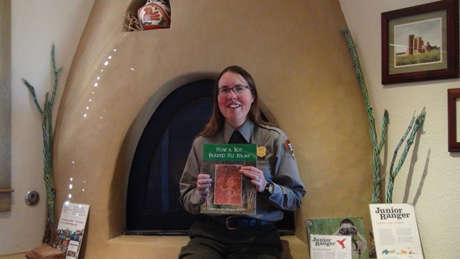 A Ranger reads "How a Boy Earned His Name" by Susan Holland while sitting in front of the fireplace.