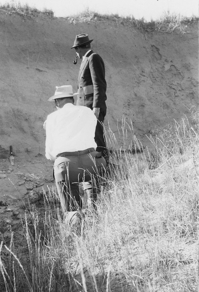 Two archeologists inspect an area of land.