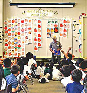 Ranger showing an exhibit to a classroom full of students. Two students are raising their hands.