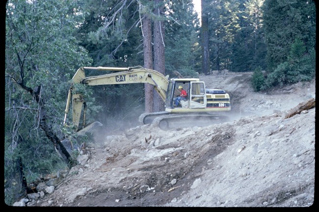 Excavator reworks the grade of a steep hill