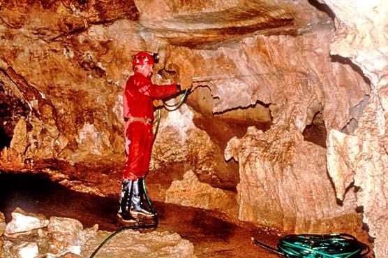 Cave specialist in red suit sprays water to clean a cave formation