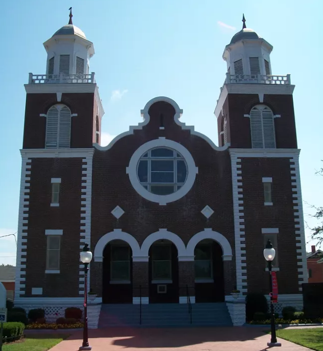 A tall brick church building with a circular window in the middle and wide brick steps.