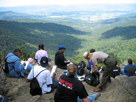 A group of Camp S.E.E.D. participants and a park ranger enjoy a spectacular valley view from a rocky cliff.