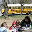 A group of students in the park with a school bus in the background.