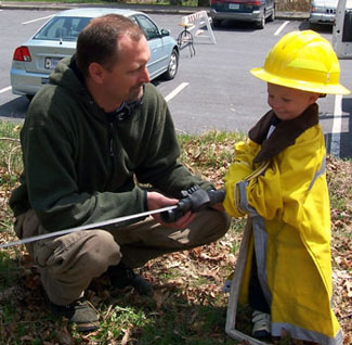 A fireman helps a young boy receive hands-on experience with a real fire hose.