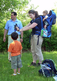 A mother receives guidance for carrying her toddler in a backpack carrier.