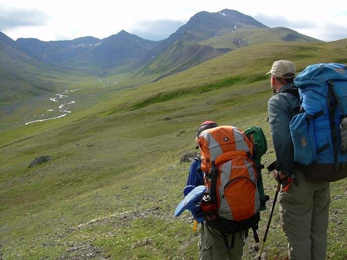 Hikers follow the historic Telaquana Trail in Lake Clark National Park & Preserve, looking out over an alpine meadow with mountains in the background.