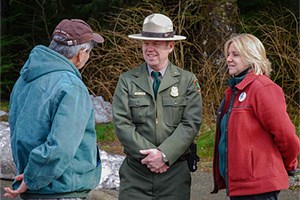 Visitors speaking with a park ranger outside, with forest in the background.