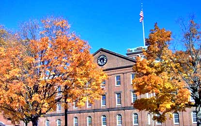 Main Arsenal building in autumn, three story brick with two trees flanking each side in orange and yellow foliage.