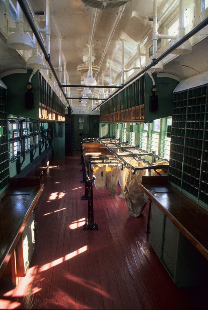 An image of the interior of the L&N #1100 Railway Post Office car, with barred windows along both sides, wooden mail sorting tables and mail holding slots