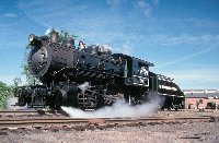 Baldwin Locomotive Works 26 is a small (90 ton) switching locomtove with a graphite smokebox (front end) and a sloped tender at the back.  It was photographed in the railroad yard with steam blowing out from its left front cylinder.
