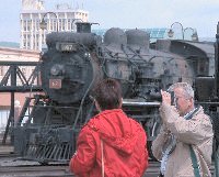 a man focuses on a locomotive out of the picture while a woman looks at a locomotive in the background