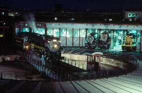 Night Photo, one steam engine on turntable (rotating bridge) and three engines with noses sticking out of roundhouse.