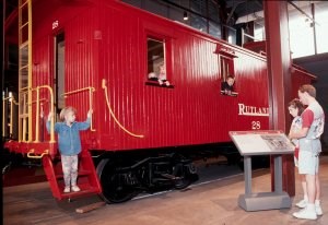 A child steps from a bright red Rutland Railroad wooden caboose on display in the Techhology Museum.