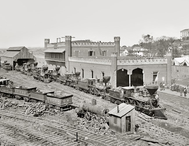 A steam locomotive and cars sits in front of brick building.