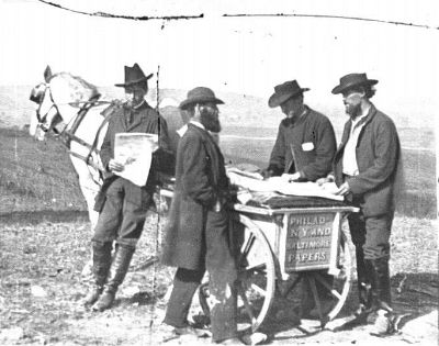 Four men standing at a horse drawn newspaper cart