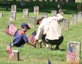 A cubscout and his father place American flags in front of headstones.
