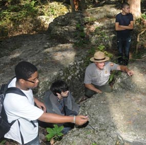 A park ranger and high school students crouch behing limestone boulders in the Slaughter Pen.