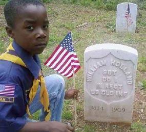 A cub scout places a flag at soldier's grave site.
