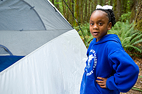 A little girl stands next to a tent