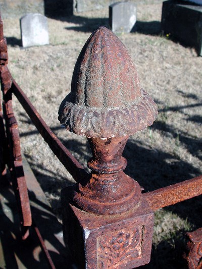 A domed iron finial at the corner of a railing is red with rust.