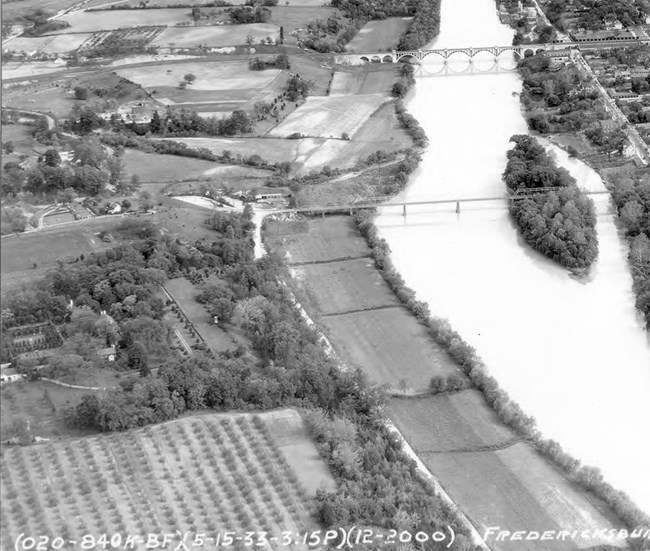 Aerial view shows Chatham Manor on the left bank of a river. The large house is surrounded by orchards and gardens.